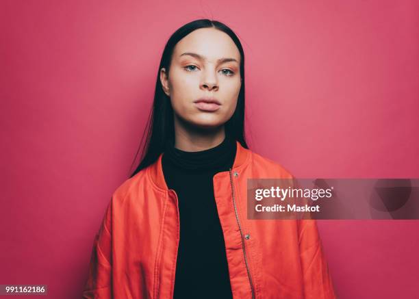 portrait of confident woman wearing orange jacket over pink background - colour background cool portrait photography stockfoto's en -beelden