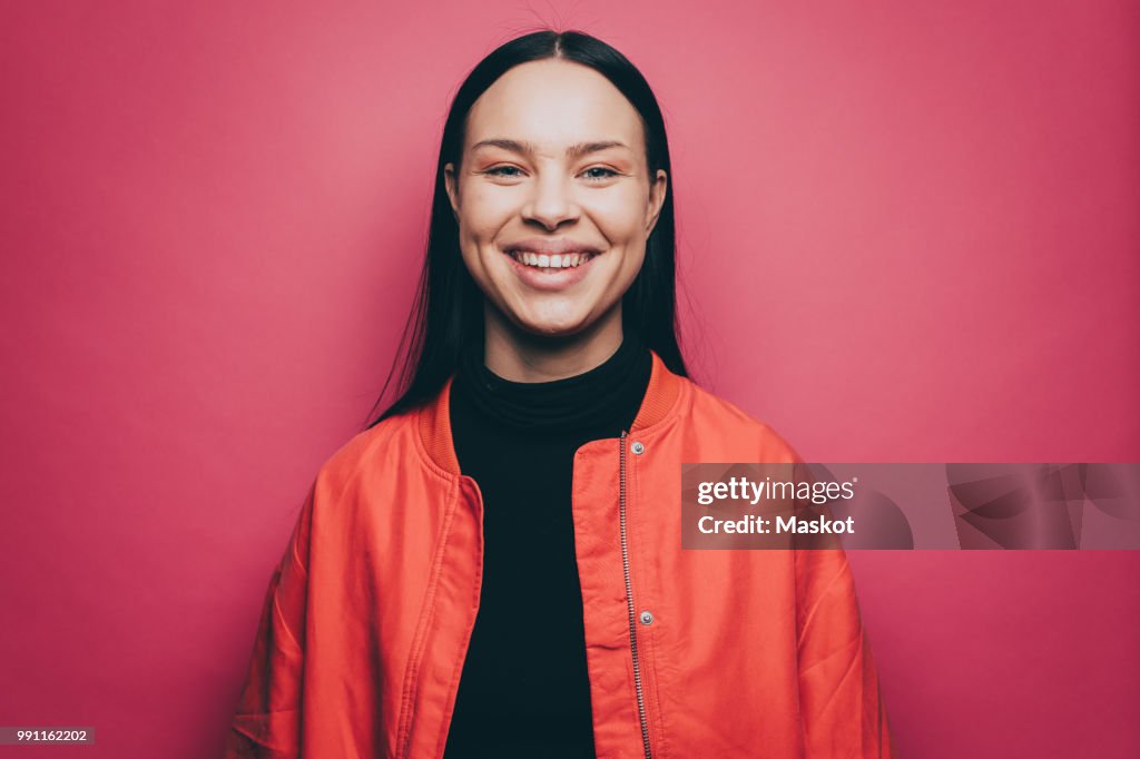 Portrait of smiling woman wearing orange jacket over pink background