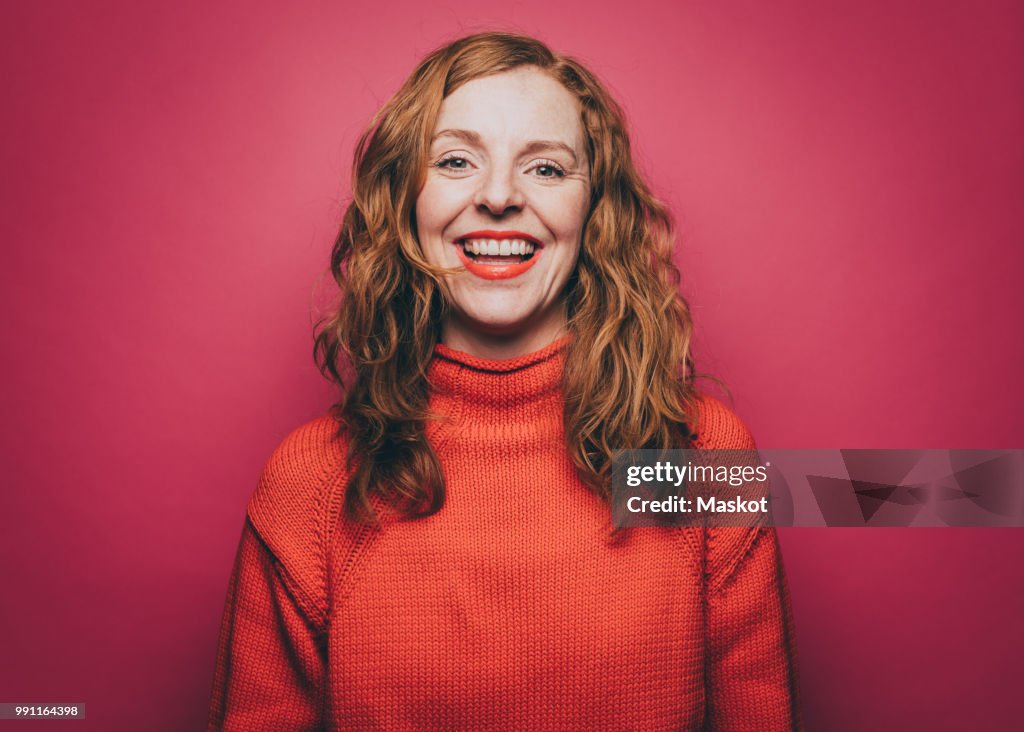 Portrait of smiling woman in orange top against pink background