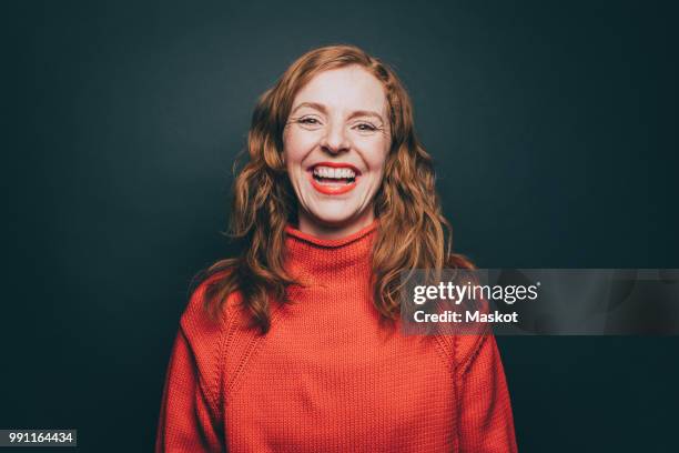 portrait of woman in orange top laughing against gray background - adulto de mediana edad fotografías e imágenes de stock