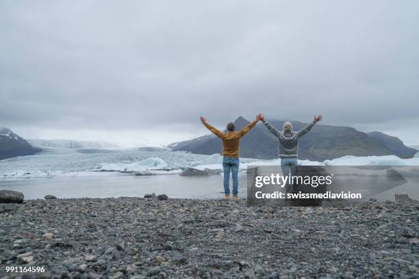young couple enjoying freedom arms outstretched at glacier lagoon, carefree vacations - south east iceland stock pictures, royalty-free photos & images