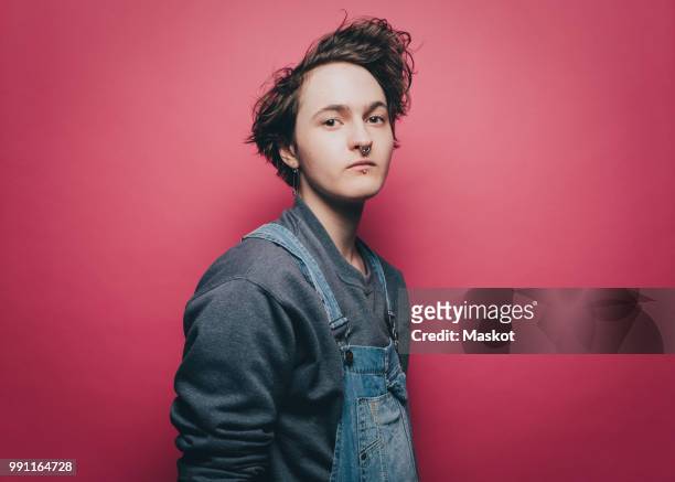 portrait of confident male hipster standing against pink background - bib overalls 個照片及圖片檔