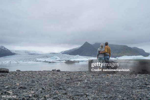 young couple contemplating glacier lagoon, embracing each other - south east iceland stock pictures, royalty-free photos & images