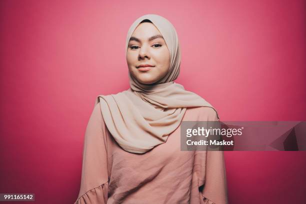 portrait of confident young woman wearing hijab against pink background - islam stock-fotos und bilder