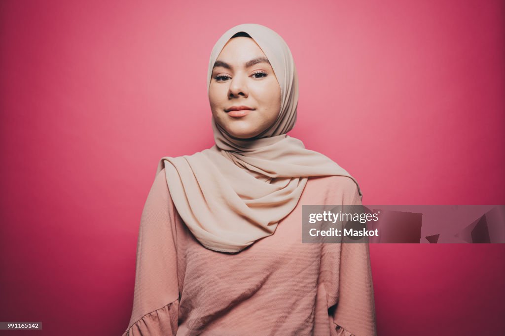 Portrait of confident young woman wearing hijab against pink background