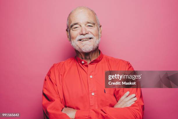 portrait of smiling senior man with arms crossed against pink background - senior studio portrait stockfoto's en -beelden