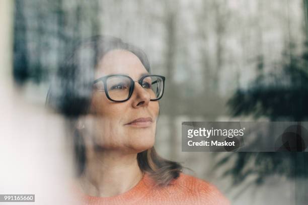 close-up of thoughtful businesswoman wearing eyeglasses seen through window - reflective stockfoto's en -beelden