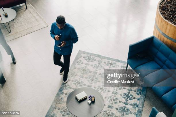 high angle view of young businessman using smart phone while walking at office - smart communicate elevation view stockfoto's en -beelden