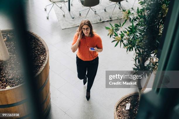 high angle view of businesswoman using mobile phone while walking in office - high angle view walking stock pictures, royalty-free photos & images