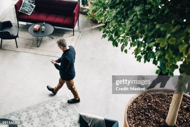 high angle view of mature businessman using mobile phone while walking in office - business scandinavia stock pictures, royalty-free photos & images