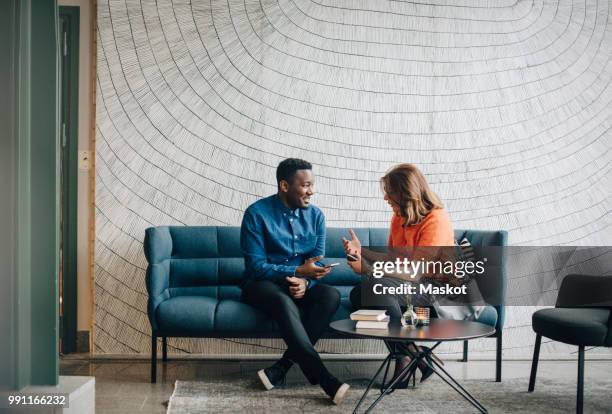 businessman and woman taking while sitting on couch against wall at conference - business people on phone ストックフォトと画像