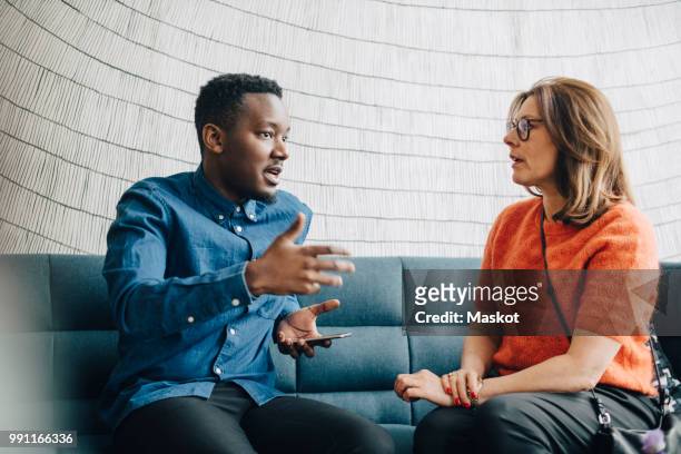 businessman sharing ideas with female colleague while sitting on couch at conference - explaining stock pictures, royalty-free photos & images