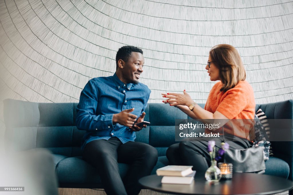 Businessman and woman using mobile phones while sitting on couch during conference