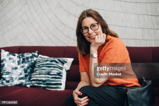 portrait of smiling mature businesswoman sitting on couch at office - businesswoman couch fotografías e imágenes de stock
