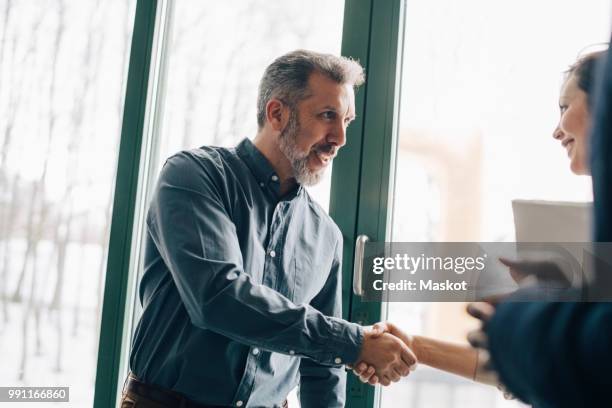 mature businessman greeting female coworker in meeting at office - global entry stock-fotos und bilder