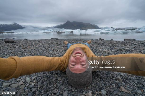 young man taking upside down selfie with glacier lake, icebergs floating on water - south east iceland stock pictures, royalty-free photos & images