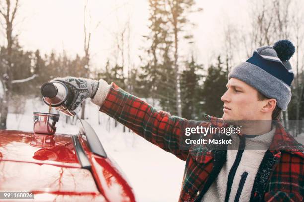 man pouring coffee from insulated drink container while standing by car during winter - coffee drink stock pictures, royalty-free photos & images