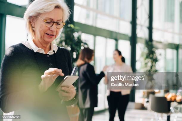 senior entrepreneur using mobile phone while coworkers discussing in background - werkende bejaarden stockfoto's en -beelden