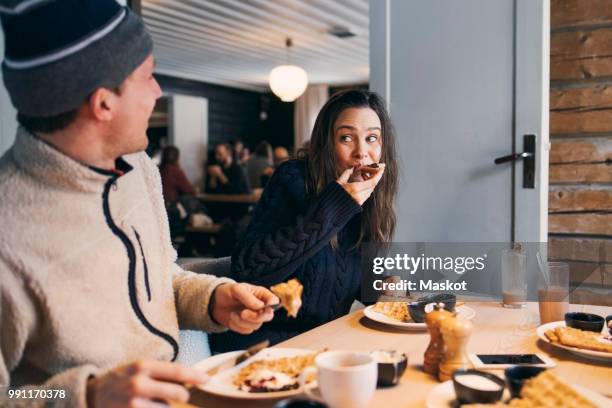 woman eating breakfast while sitting with friend at table in log cabin - waffles stock pictures, royalty-free photos & images