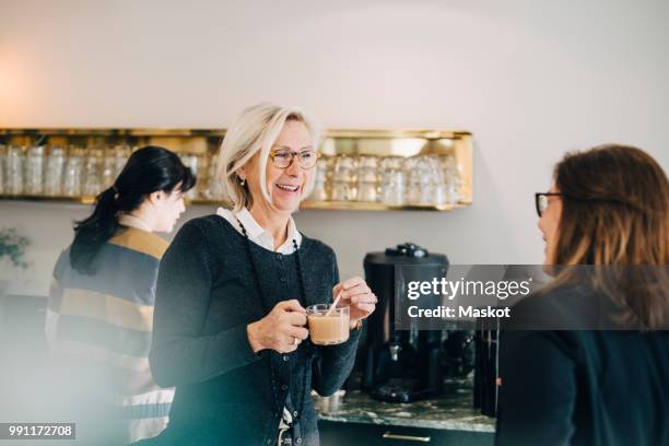 businesswoman having tea while talking to coworker at office - pause café bureau photos et images de collection