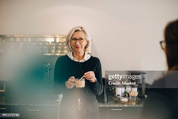 businesswoman looking at colleague while making tea in office - coffee break office stock-fotos und bilder