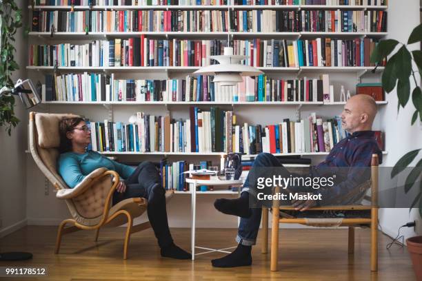 full length of therapist and patient discussing by bookshelf at home office - psychiatrists couch fotografías e imágenes de stock