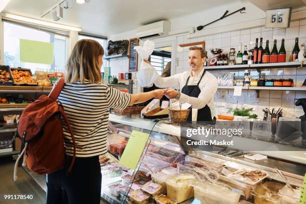 male sales clerk holding plastic bag while accepting credit card from customer at checkout counter - convenient store stock pictures, royalty-free photos & images