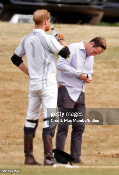 Prince Harry, Duke of Sussex drinks a bottle of water whilst he has his sunglasses cleaned for him by his polo manager Andrew Tucker during the Audi...