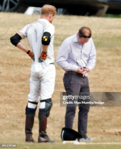 Prince Harry, Duke of Sussex stretches his back whilst he has his sunglasses cleaned for him by his polo manager Andrew Tucker during the Audi Polo...