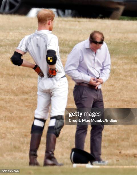 Prince Harry, Duke of Sussex stretches his back whilst he has his sunglasses cleaned for him by his polo manager Andrew Tucker during the Audi Polo...