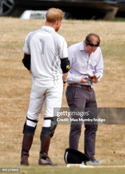 Prince Harry, Duke of Sussex looks on as he has his sunglasses cleaned for him by his polo manager Andrew Tucker during the Audi Polo Challenge at...