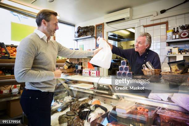 male sales clerk handing over bag to customer at counter in store - plastic bag stock pictures, royalty-free photos & images