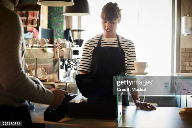 female barista using cash register with customer in foreground at cafe - pay day stock pictures, royalty-free photos & images