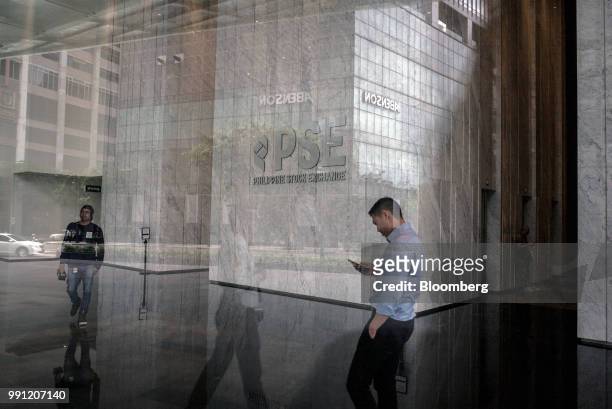 Man looks at a mobile phone as signage for Philippine Stock Exchange Inc. Is displayed in the lobby of the bourse in Bonifacio Global City , Metro...