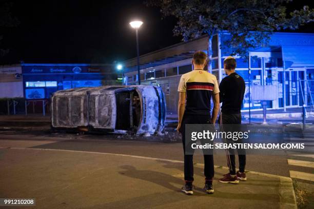 Residents look at a burnt car in the Breil neighborhood of Nantes early on July 4, 2018. Groups of young people clashed with police in the western...