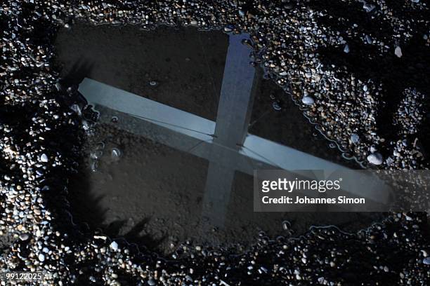 The monumental main cross, symbolizing the Christian faith, is silhouetted in a puddle at the Theresienwiese during dusk of day 1 of the 2nd...