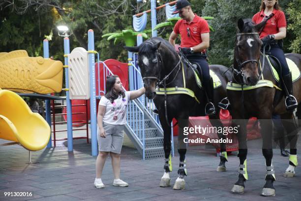 Girl pats the horse of a mounted policeman as they patrol at a playground in Turkish capital Ankara on July 04, 2018.