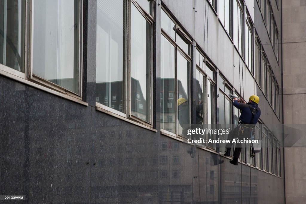Absailing Window Cleaner An abseiling window cleaner cleaning the windows of the office block ...