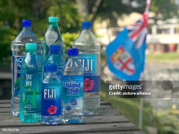 Different brand bottles of still mineral water from the Fiji Islands are on display on a table in front of the Fiji national flag on the island of...