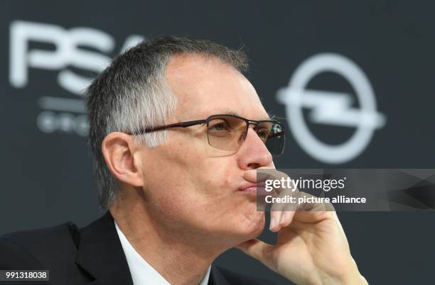 The chairman of PSA Peugeot Citroen Carlos Tavares sits in front of the companies' logos - PSA and Opel - and looks on the crowd during the press...