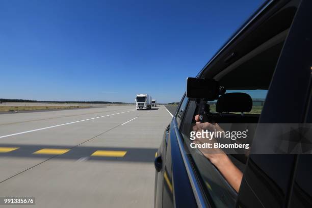 Journalist films from an automobile passenger window as a pair of MAN SE TGX freight trucks drive during a wireless communication technology...