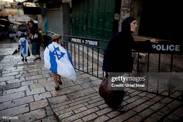 Palestinian woman walks past Israeli children covered with their national flag as Israelis take part in a march marking Jerusalem Day on May 12,...