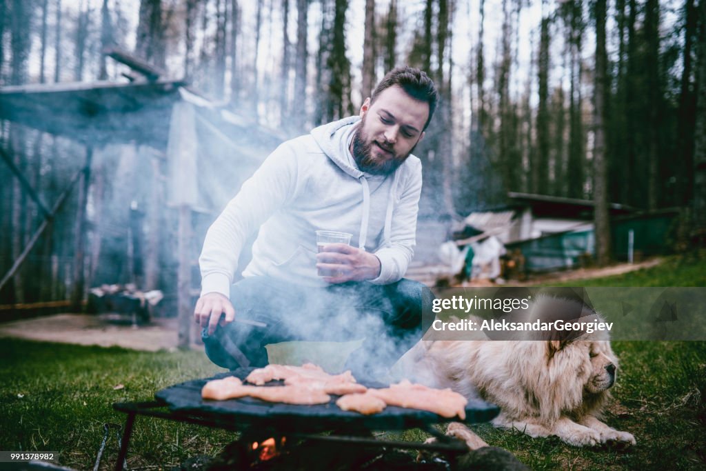 Beau mâle faire Barbecue tandis qu’animal chien repose à côté de lui