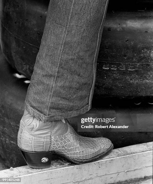 Driver Richard Petty, his cowboy boots embellished with the logo of his racecar's sponsor, STP, stands in the garage prior to the start of the 1982...