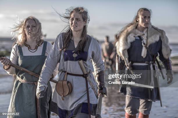 drie vrouwelijke vikingen poseren voor een groep van krijgers stond in de branding op de kust - viking stockfoto's en -beelden