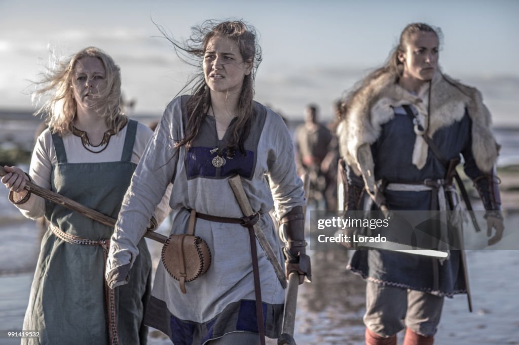 Three female vikings posing in front of a group of warriors stood in the surf on the shore