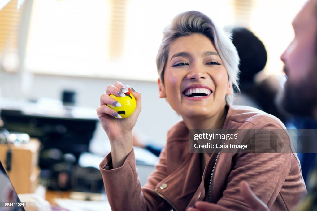 Laughing creative businesswoman squeezing stress ball in office