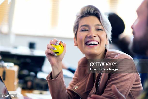 laughing creative businesswoman squeezing stress ball in office - vanguardians stock pictures, royalty-free photos & images