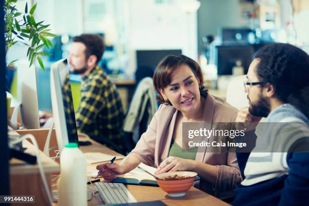 creative business people eating cereal, meeting at computer in open plan office - vanguardians stock-fotos und bilder