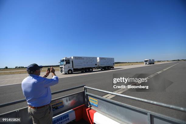 An attendee takes a photo as a pair of MAN SE TGX freight trucks pass by during a wireless communication technology "platooning" test drive on a...